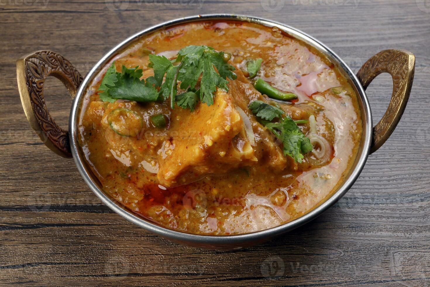 Haleem stew wheat barley lentils mutton goat chicken beef meat bone spice served in a copper brass pot over rustic wood background photo