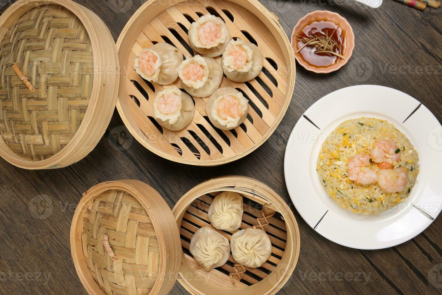 Prawn shrimp shaomai Xiao long bao dim sum dumpling chicken prawn fish seafood vegetable in bamboo steamer fried rice on plate sauce chopsticks soup spoon over rustic background photo