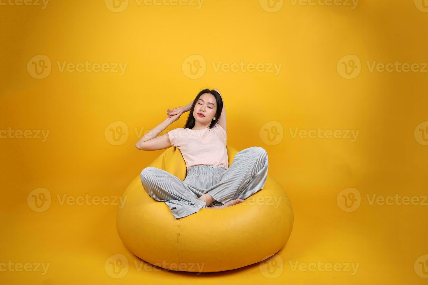 Beautiful young south east Asian woman sits on a yellow beanbag seat orange yellow color background pose fashion style elegant beauty mood expression rest relax exercise stretch yoga photo