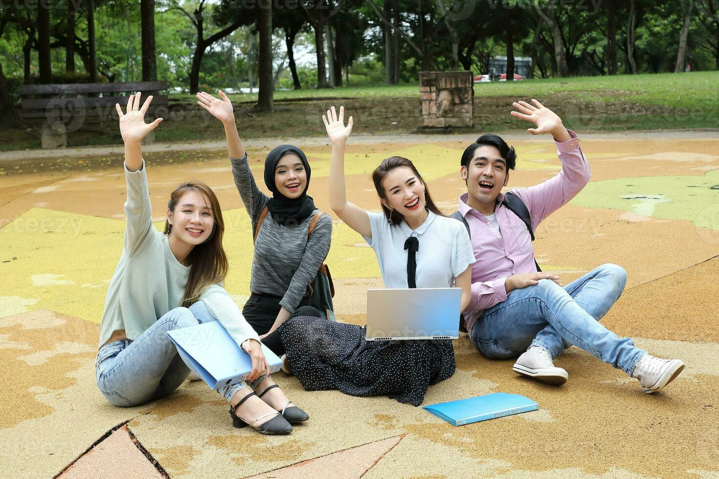 Young asian malay chinese man woman outdoor park sit on ground study talk discuss point laptop file book backpack mingle fun wave hello greet photo