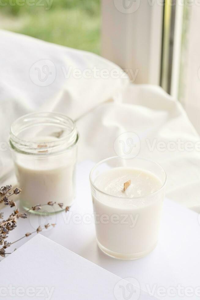 Soy wax aroma candles in jar on bed with lavender flowers. Candle mockup design photo