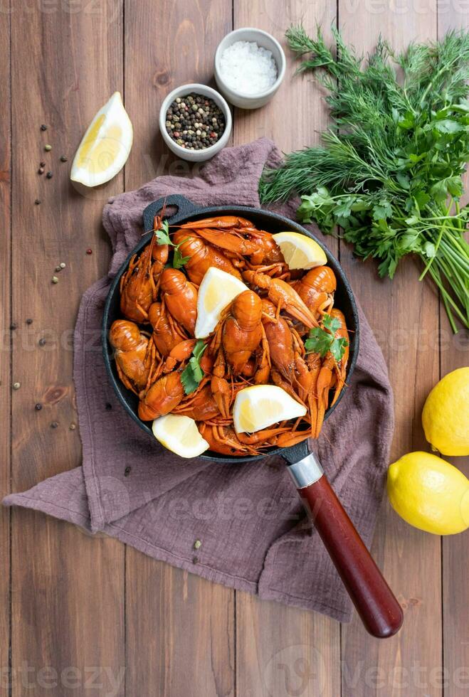 cooked crawfish in black saucepan with lemons and spices on wooden background photo