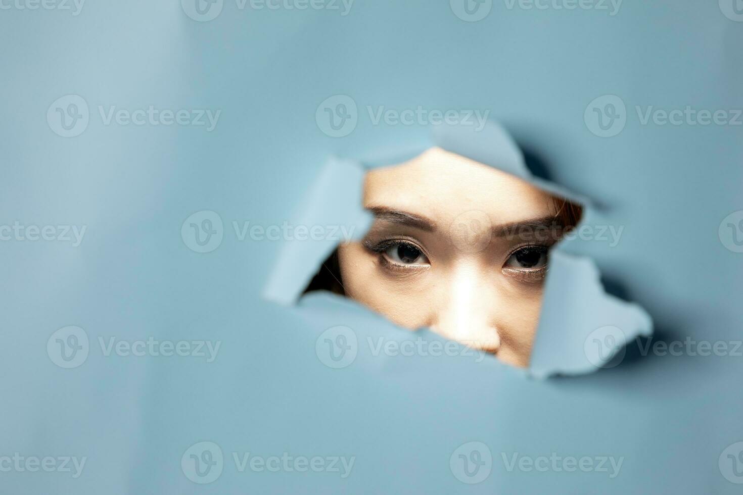 Young beautiful Asian woman expression through torn paper hole photo