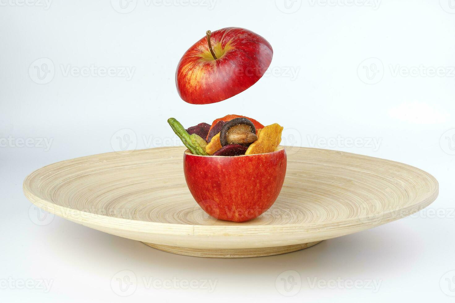 Healthy vegetable chips yellow sweet potato purple carrot green radish green beans and shiitake mushrooms in hollow red apple white background wooden plate photo