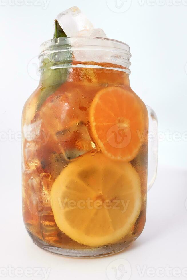 Liquid ice lemon orange tea with slice green leaf cinnamon stick in transparent glass jar mug on white background photo