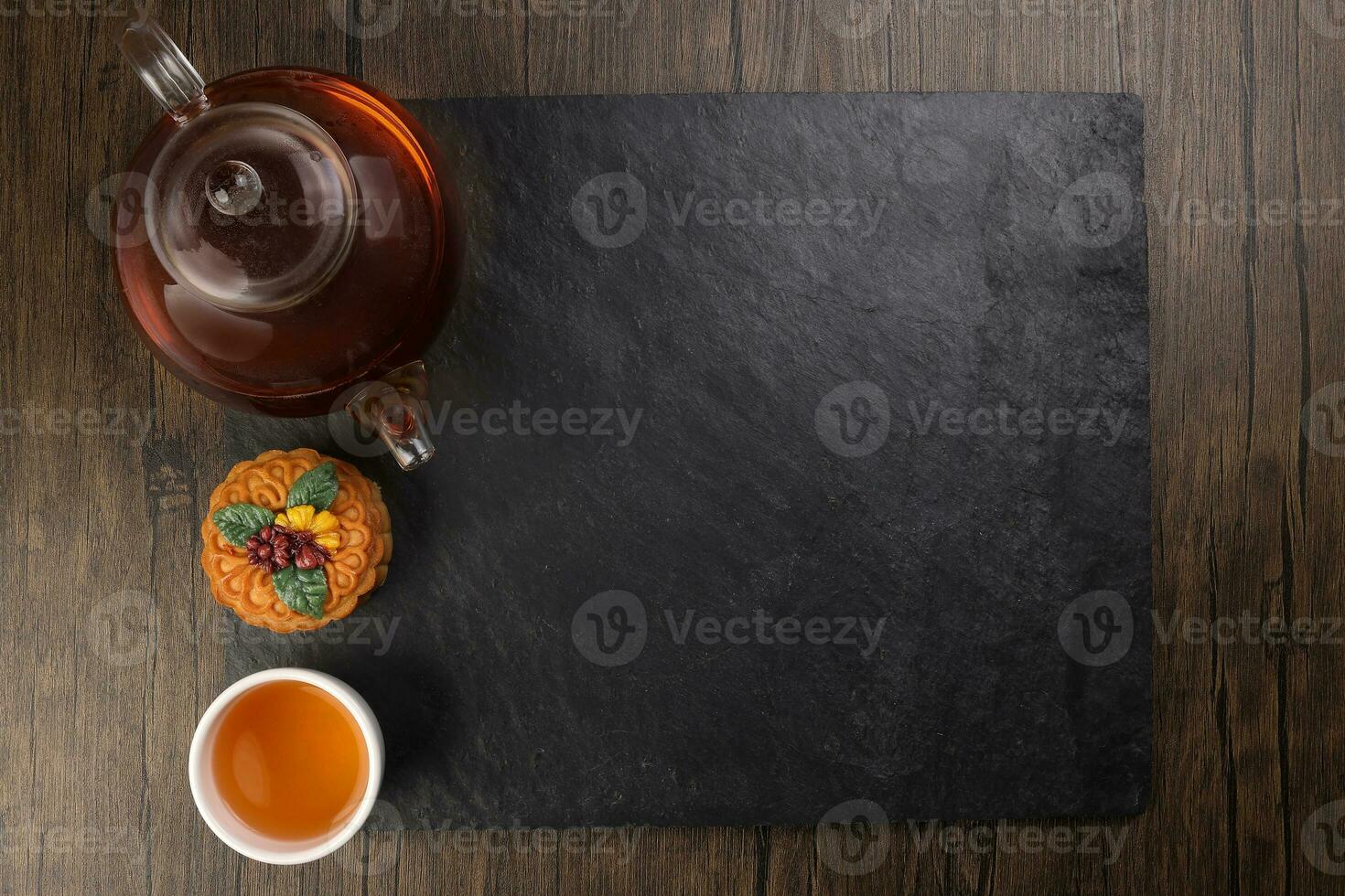 Colourful flower decorated mooncake cut slice half layer Chinese mid autumn festival on glass teapot white ceramic teacup over black slate stone border copy text space photo