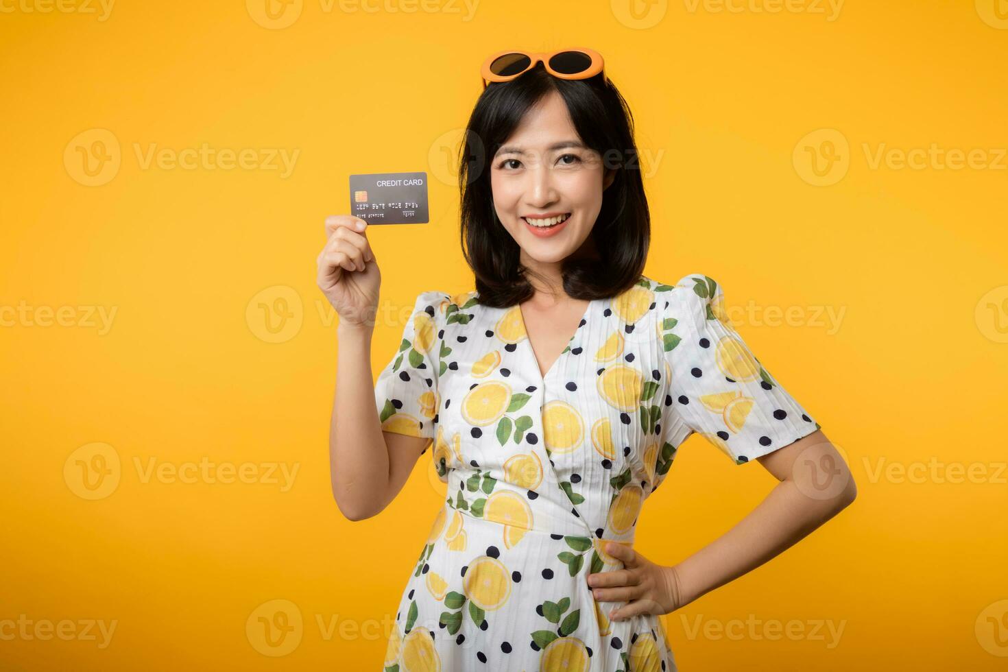 retrato joven asiático mujer contento sonriente en primavera vestir demostración el plastico crédito tarjeta aislado en amarillo antecedentes. pagar, dinero y compra compras pago concepto. foto