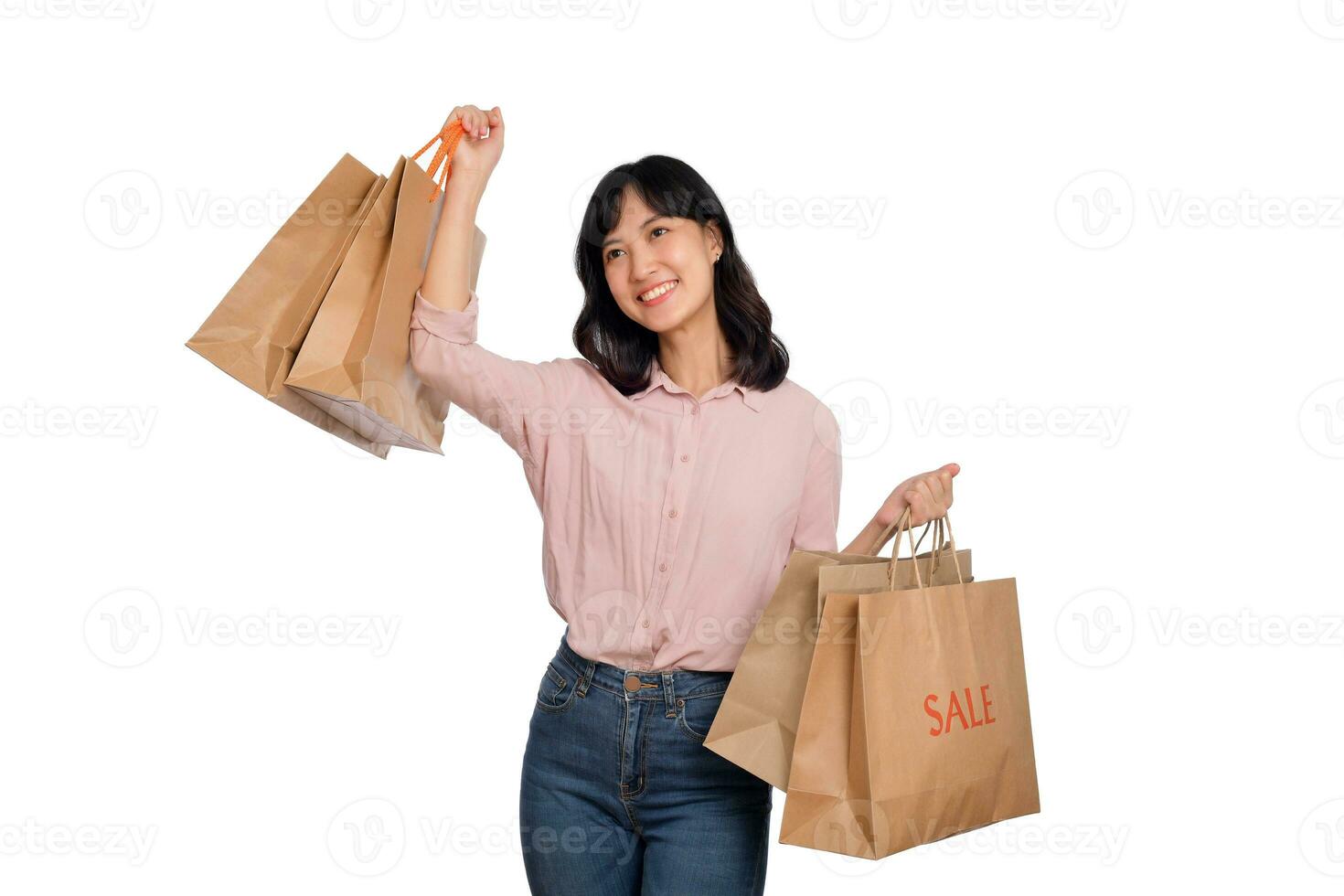 joven contento asiático mujer con casual camisa y mezclilla pantalones participación compras papel bolso aislado en blanco antecedentes foto