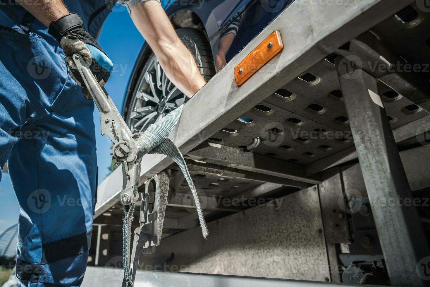 Worker Securing Car on Towing Truck with Tie Down Belts photo