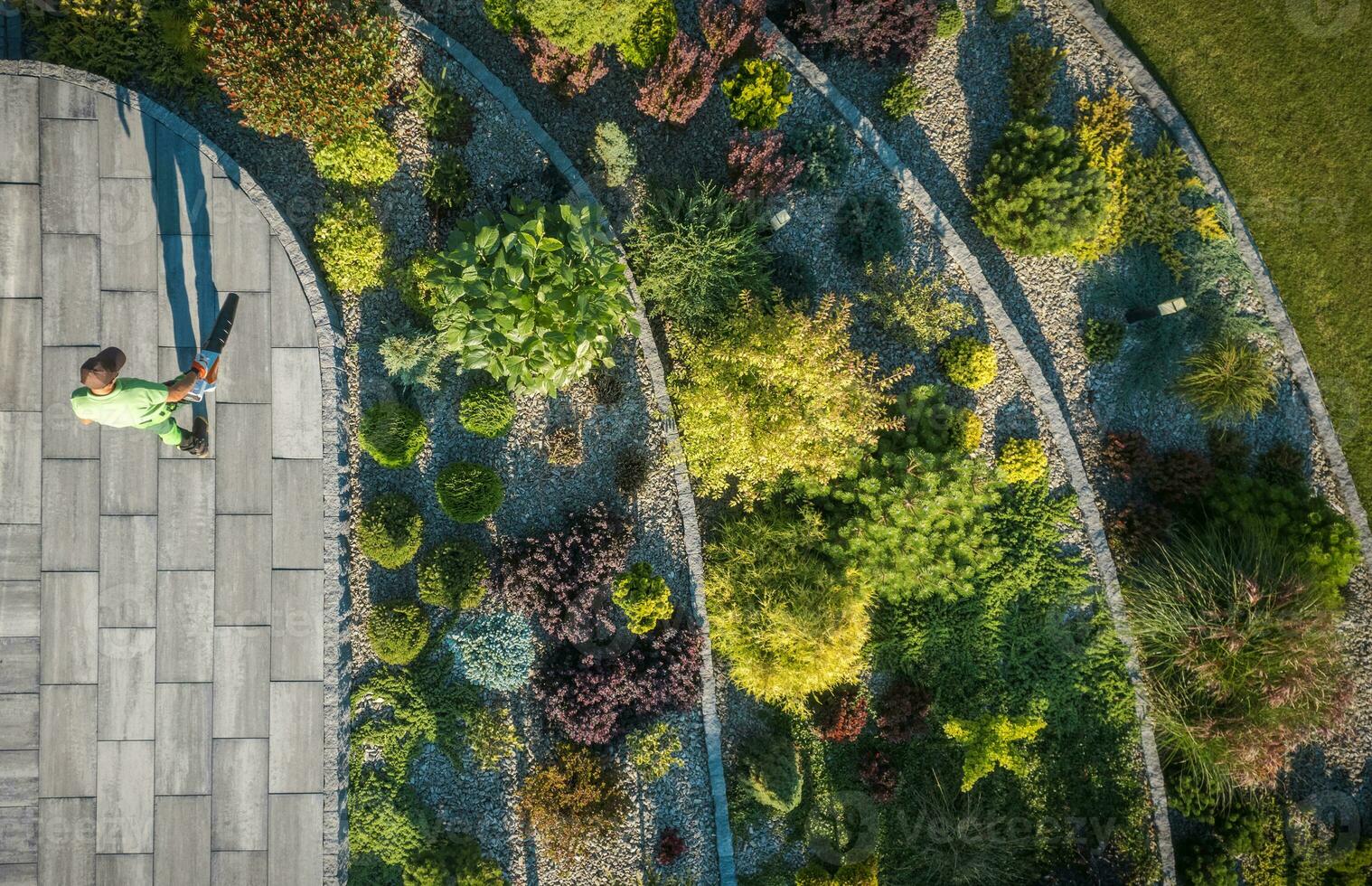Residential Rockery Backyard Garden and Man Blowing Leaves From a Path photo