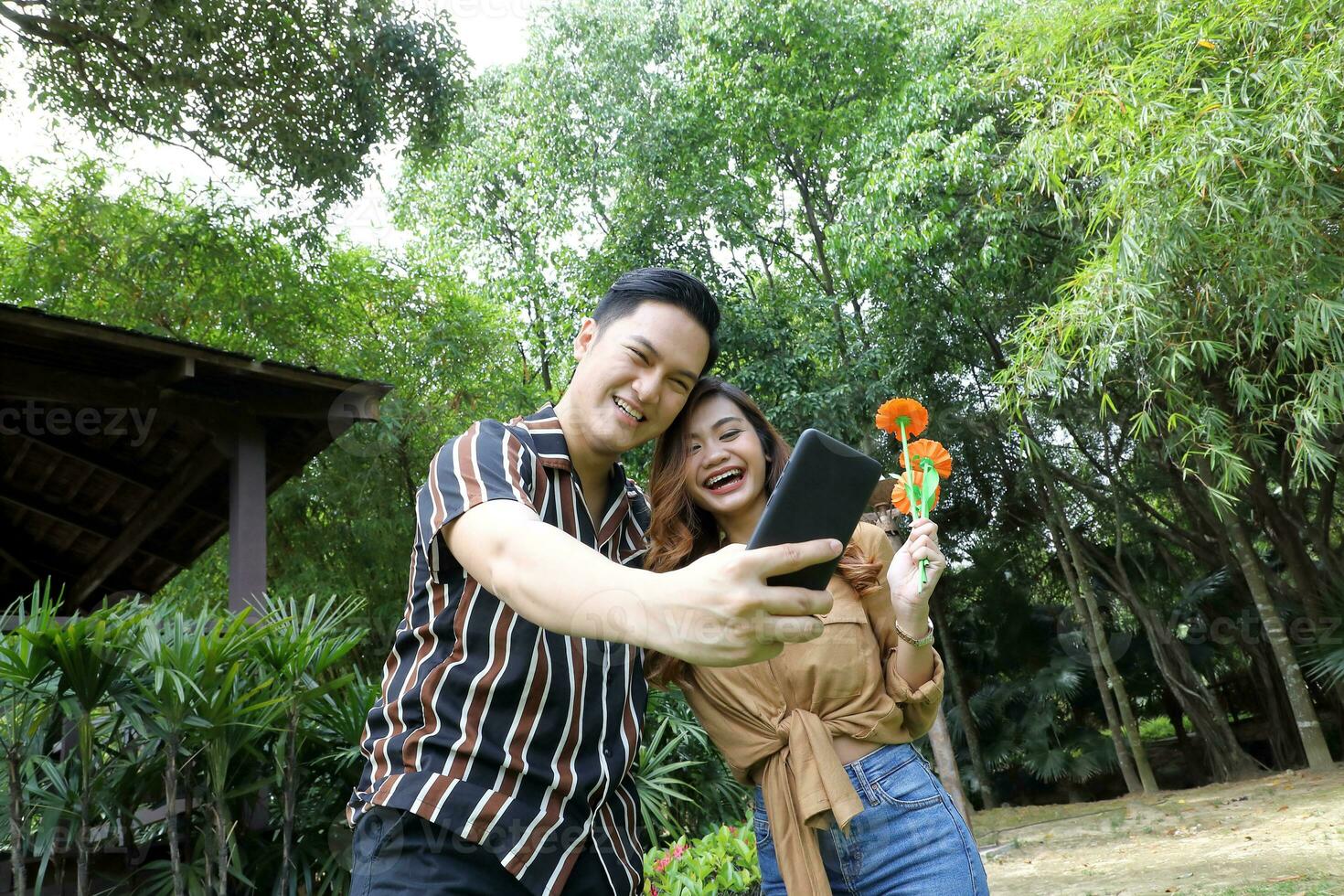 Young Asian Malay man woman outdoor green park walk talk discuss mingle under umbrella photo