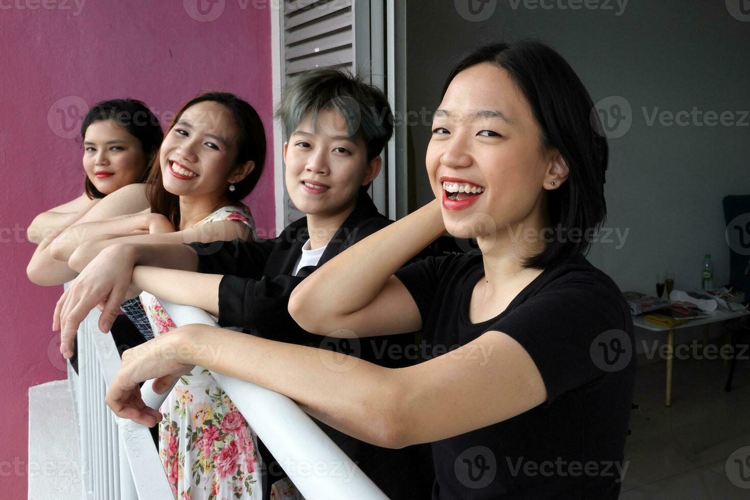 Young southeast asian woman group on balcony veranda standing side by side enjoying view talking happy looking photo