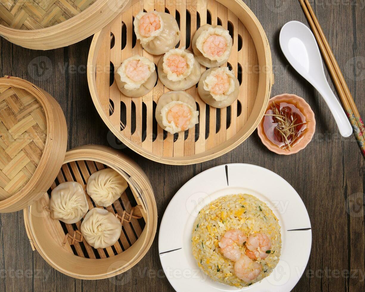 Prawn shrimp shaomai Xiao long bao dim sum dumpling chicken prawn fish seafood vegetable in bamboo steamer fried rice on plate sauce chopsticks soup spoon over rustic background photo