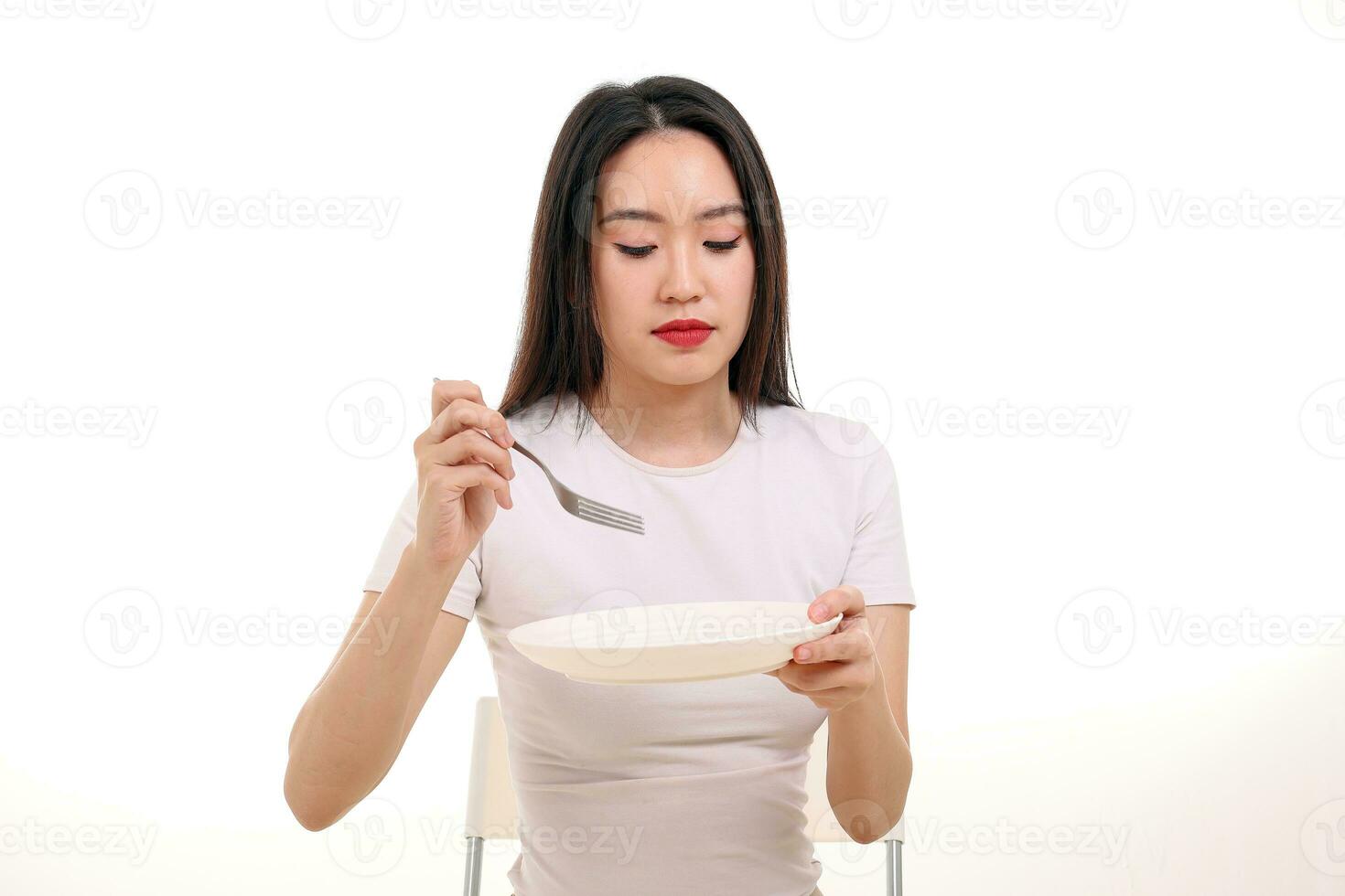 hermosa joven sur este asiático mujer participación vacío blanco plato tenedor cuchara en otro mano comer gusto Mira ver comida foto