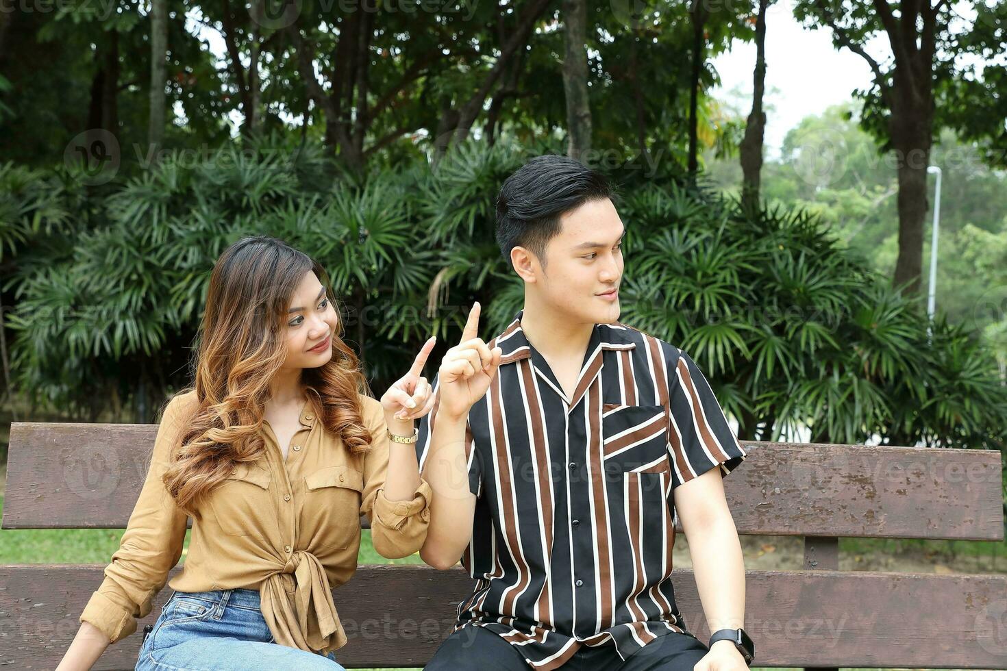 Young Asian Malay man woman outdoor green park walk talk discuss mingle under umbrella photo