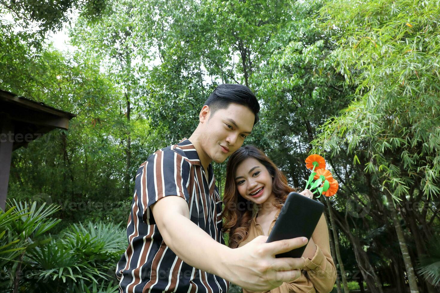 Young Asian Malay man woman outdoor green park walk talk discuss mingle under umbrella photo