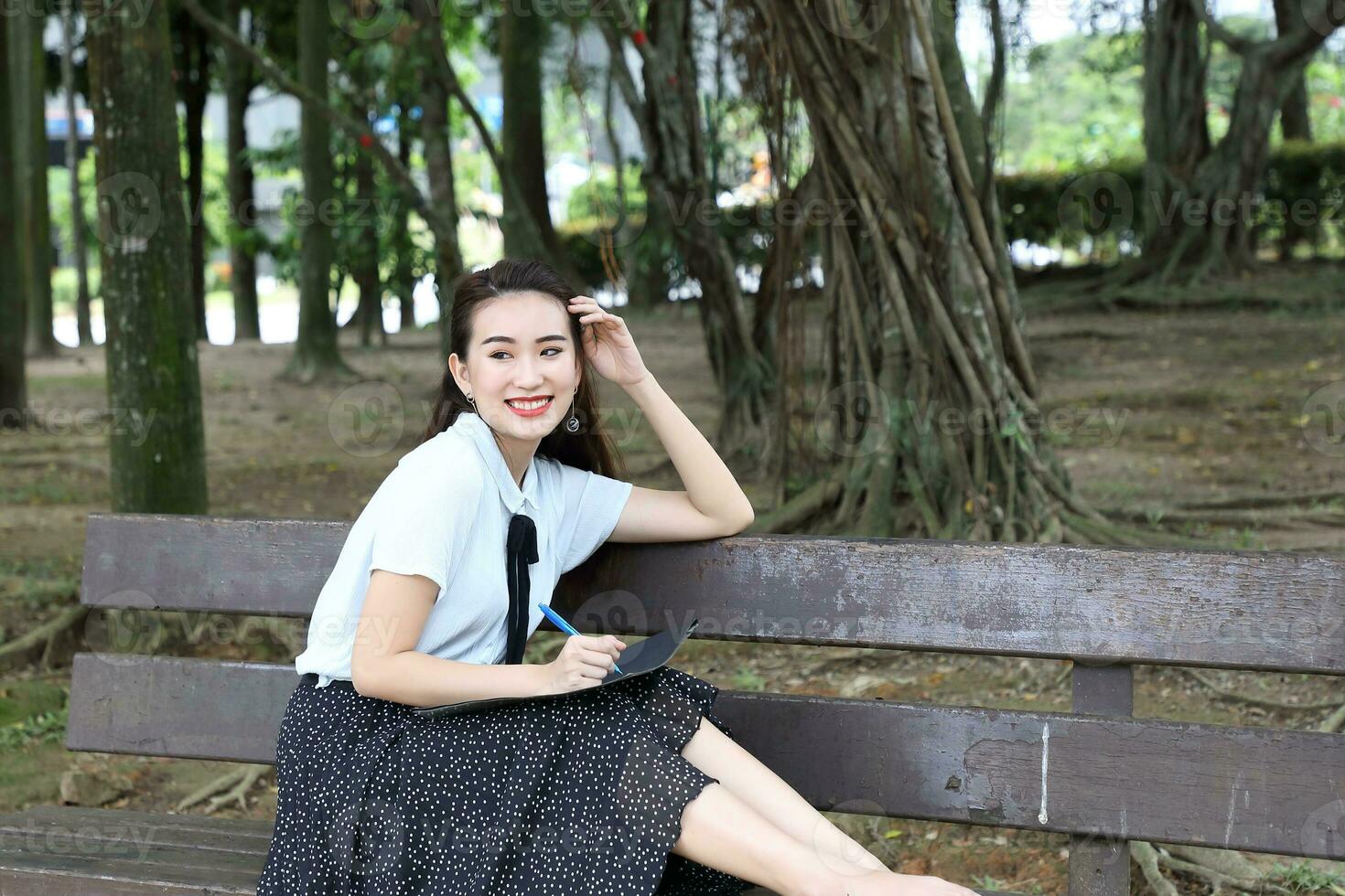 Young asian chinese woman outdoor on park bench hold file book folder read write see smile photo