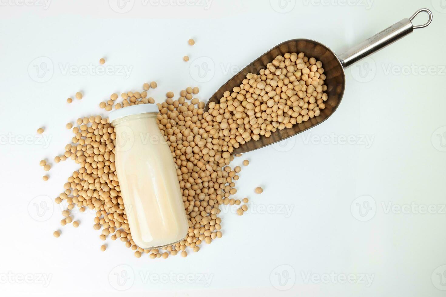 Soyabeans pouring from metal scoop around bottle of soya bean milk on white background photo