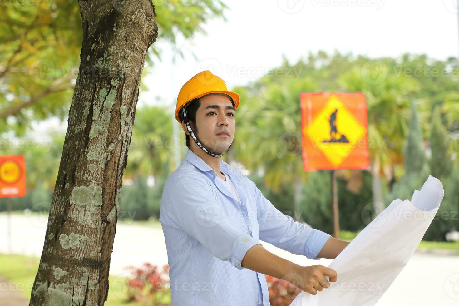 Asian man malay worker engineer management hard hat safety helmet at construction site reading seeing plan blueprint look forward photo