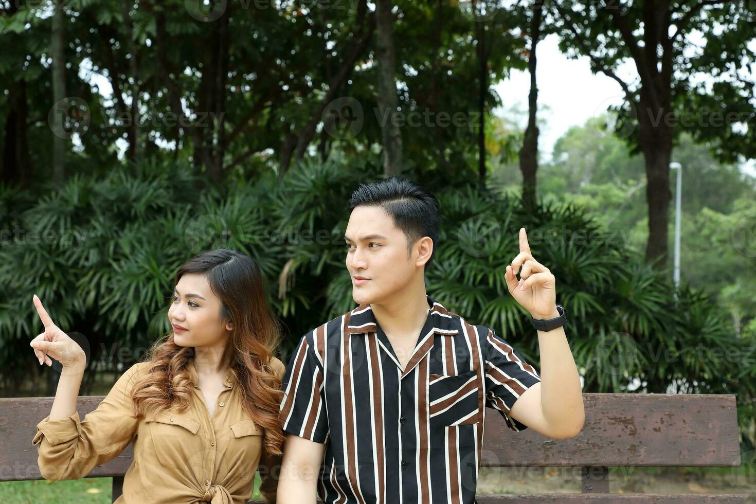 Young Asian Malay man woman outdoor green park walk talk discuss mingle under umbrella photo