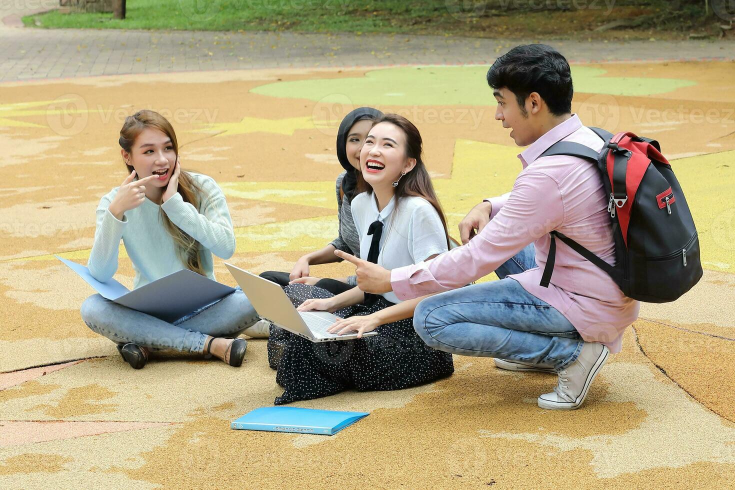 Young asian malay chinese man woman outdoor park sit on ground study talk discuss point laptop file book backpack mingle fun meet photo