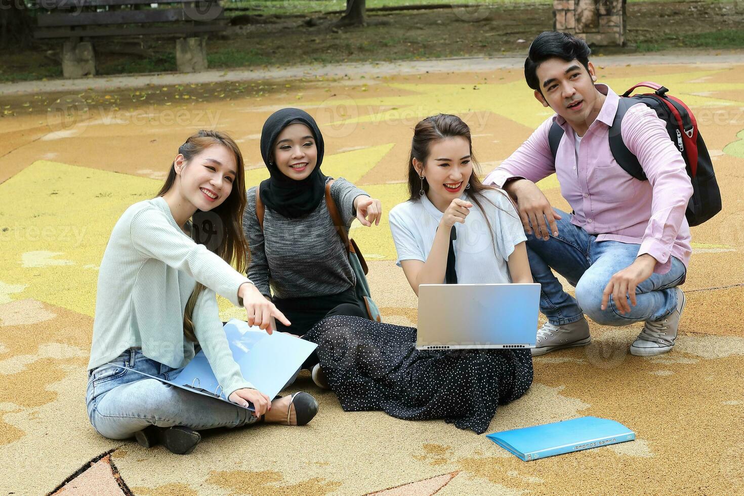 Young asian malay chinese man woman outdoor park sit on ground study talk discuss point laptop file book backpack mingle fun pint photo