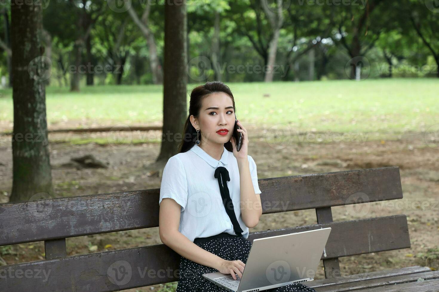 Young asian chinese woman outdoor on park bench use laptop computer think read look happy wonder smile front talk on phone photo