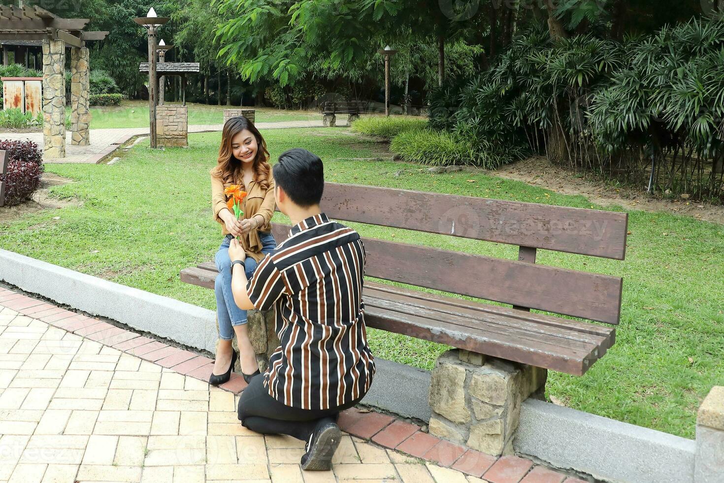 Young Asian Malay man woman outdoor green park walk talk discuss mingle under umbrella photo