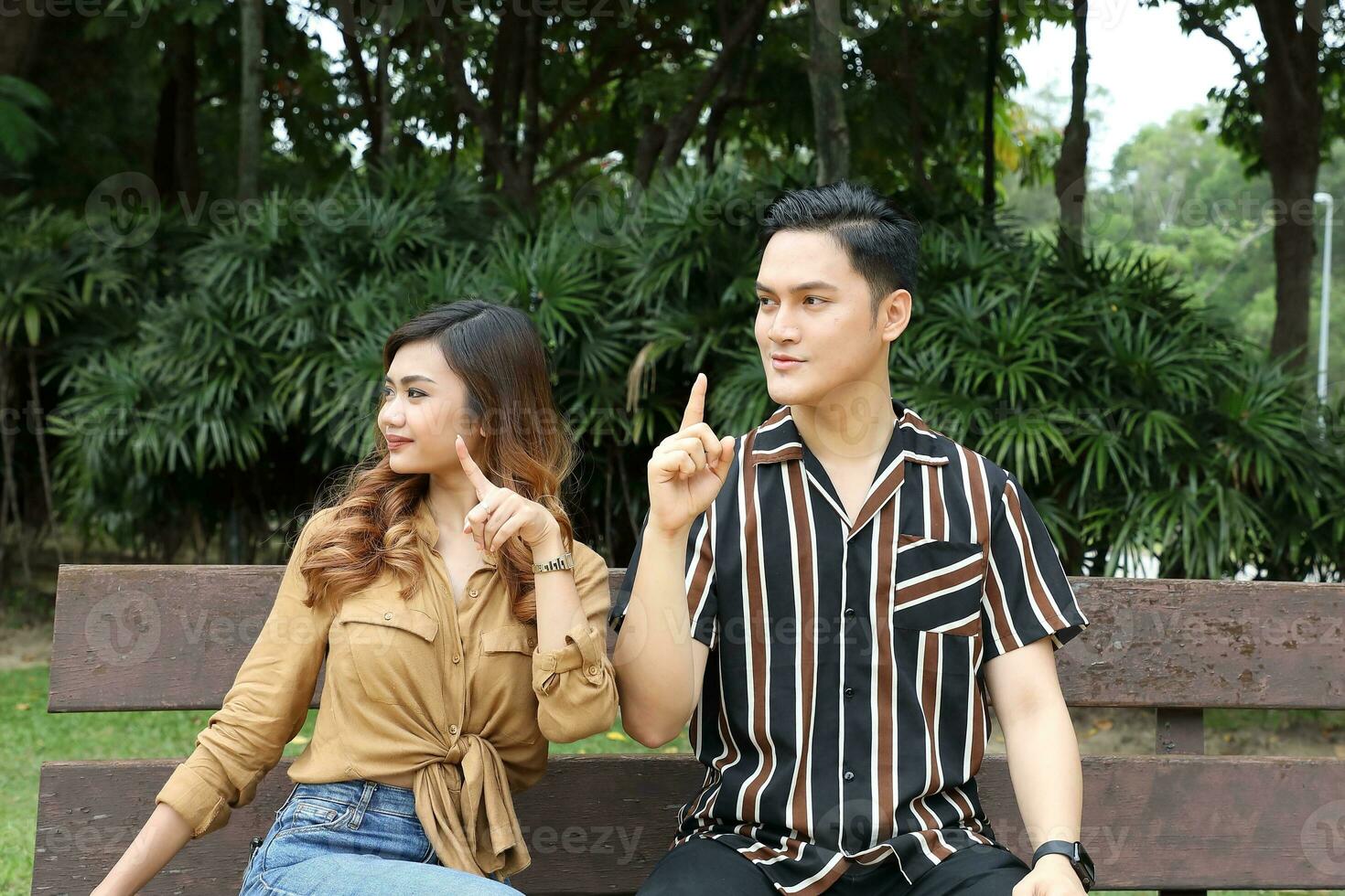 Young Asian Malay man woman outdoor green park walk talk discuss mingle under umbrella photo