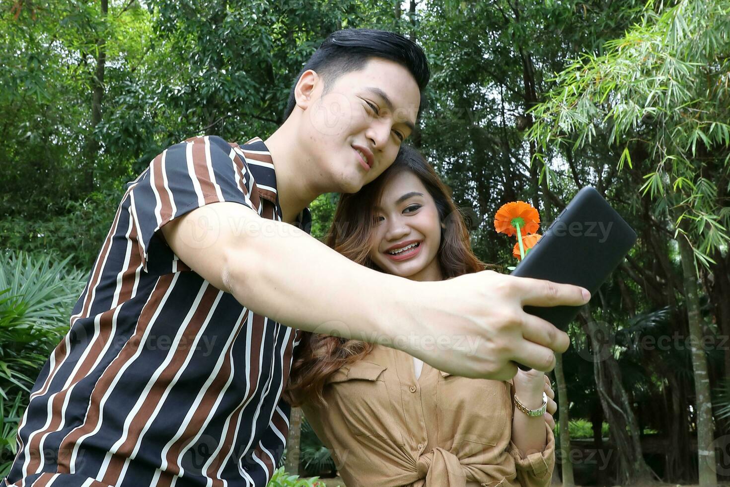 Young Asian Malay man woman outdoor green park walk talk discuss mingle under umbrella photo
