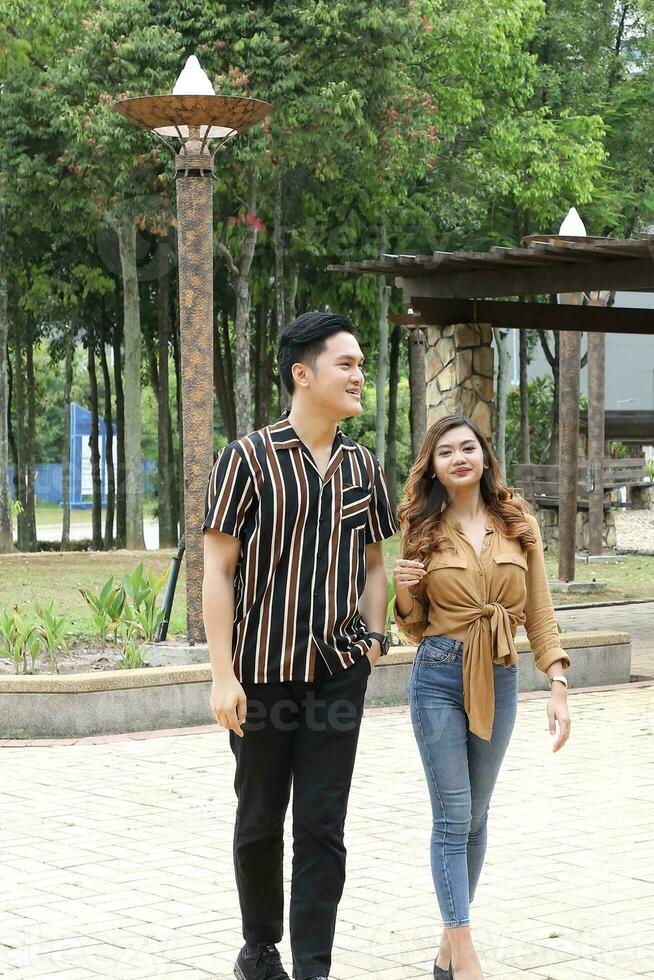 Young Asian Malay man woman outdoor green park walk talk discuss mingle under umbrella photo