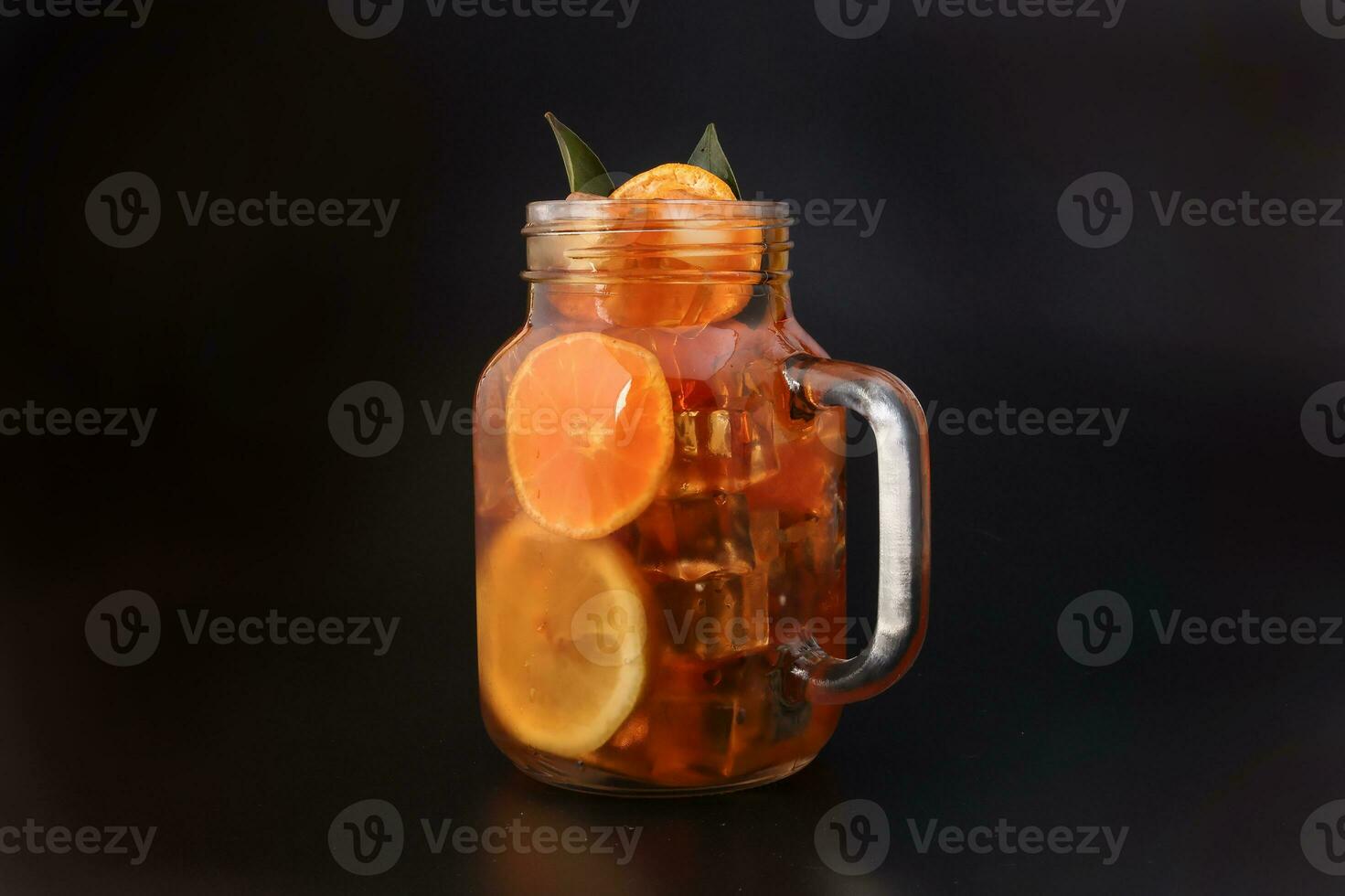 Liquid ice lemon orange tea with slice green leaf cinnamon stick in transparent glass jar mug on black background photo