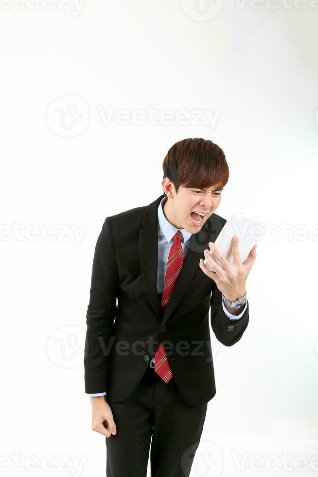 Young smart handsome Asian man business office wearing suit tie on white background looking at smartphone massage angry exited shouting photo