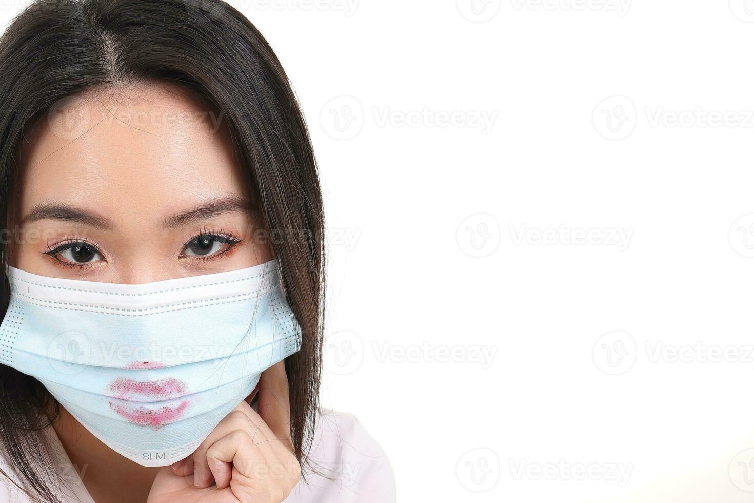 Beautiful young south east Asian woman wearing blue three ply anti virus surgical face mask lipstick lips kiss sign mark on white background look forward photo