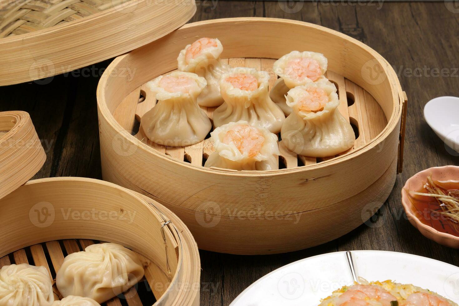 Prawn shrimp shaomai Xiao long bao dim sum dumpling chicken prawn fish seafood vegetable in bamboo steamer fried rice on plate sauce chopsticks soup spoon over rustic background photo