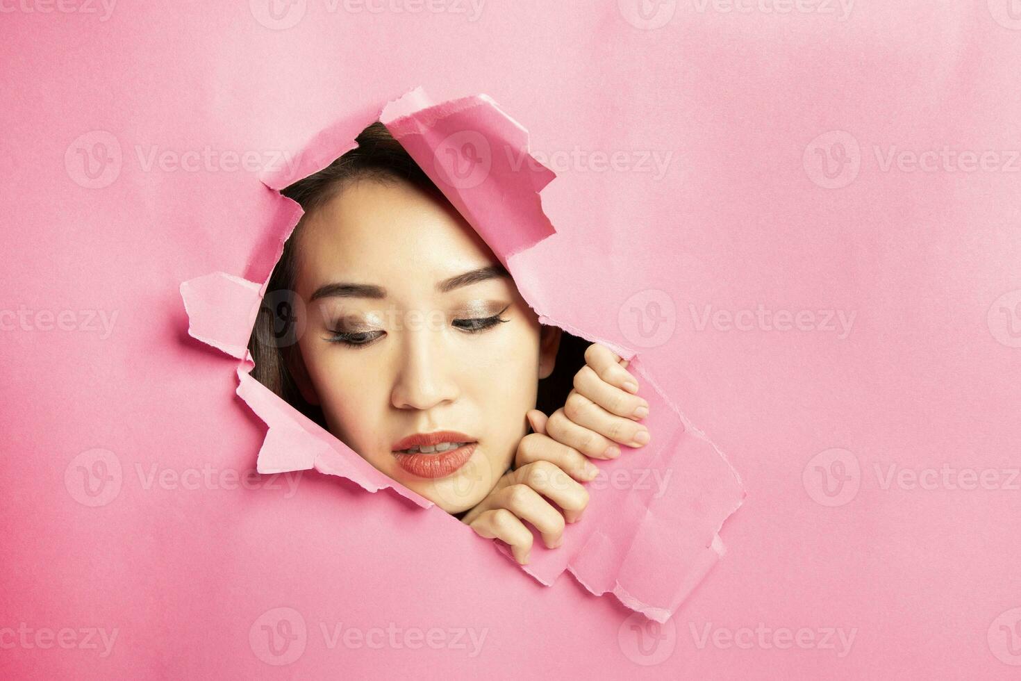 Young beautiful Asian woman expression through torn paper hole photo