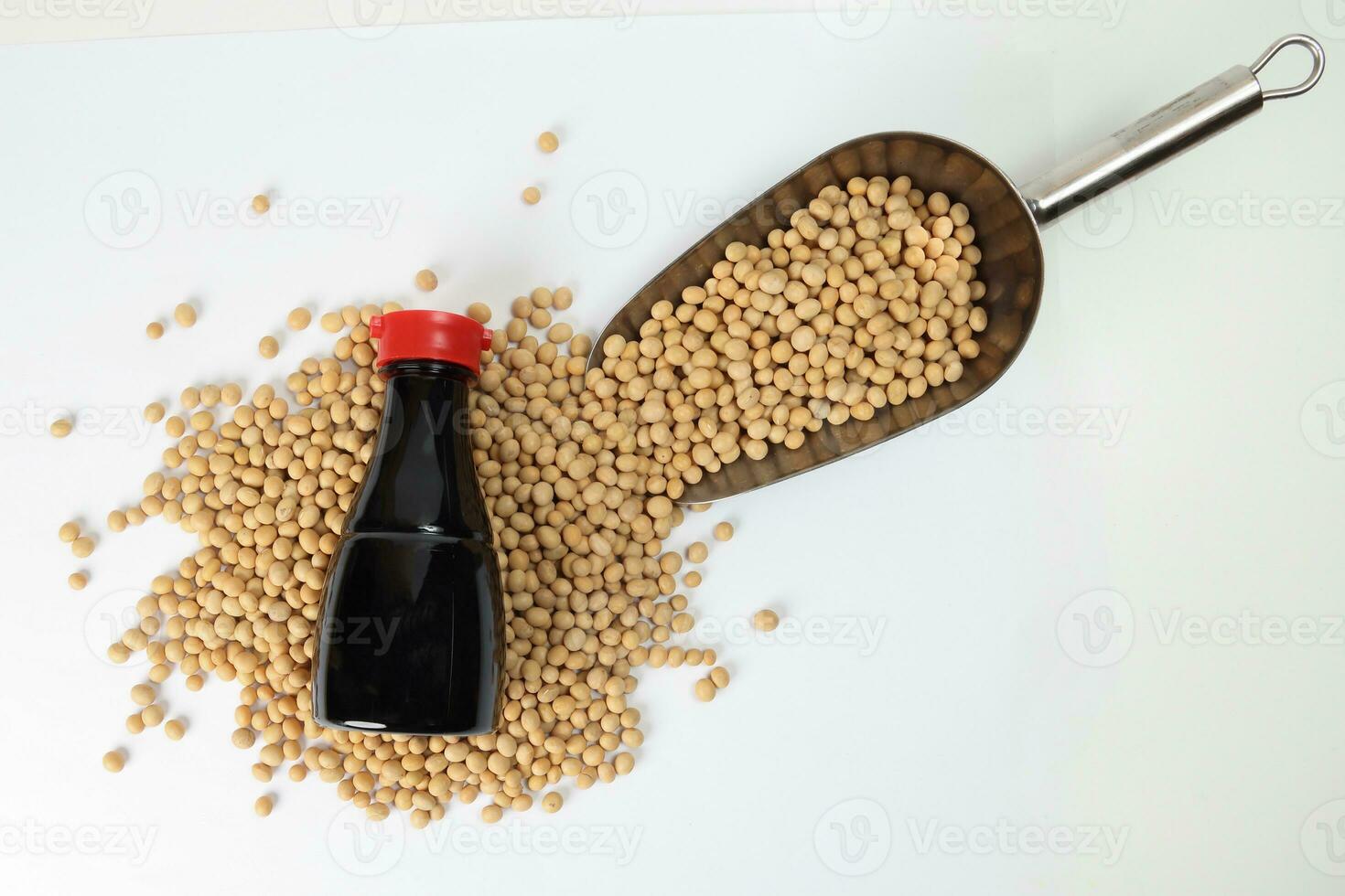 Soyabeans pouring from metal scoop around bottle of soya bean sauce on white background photo