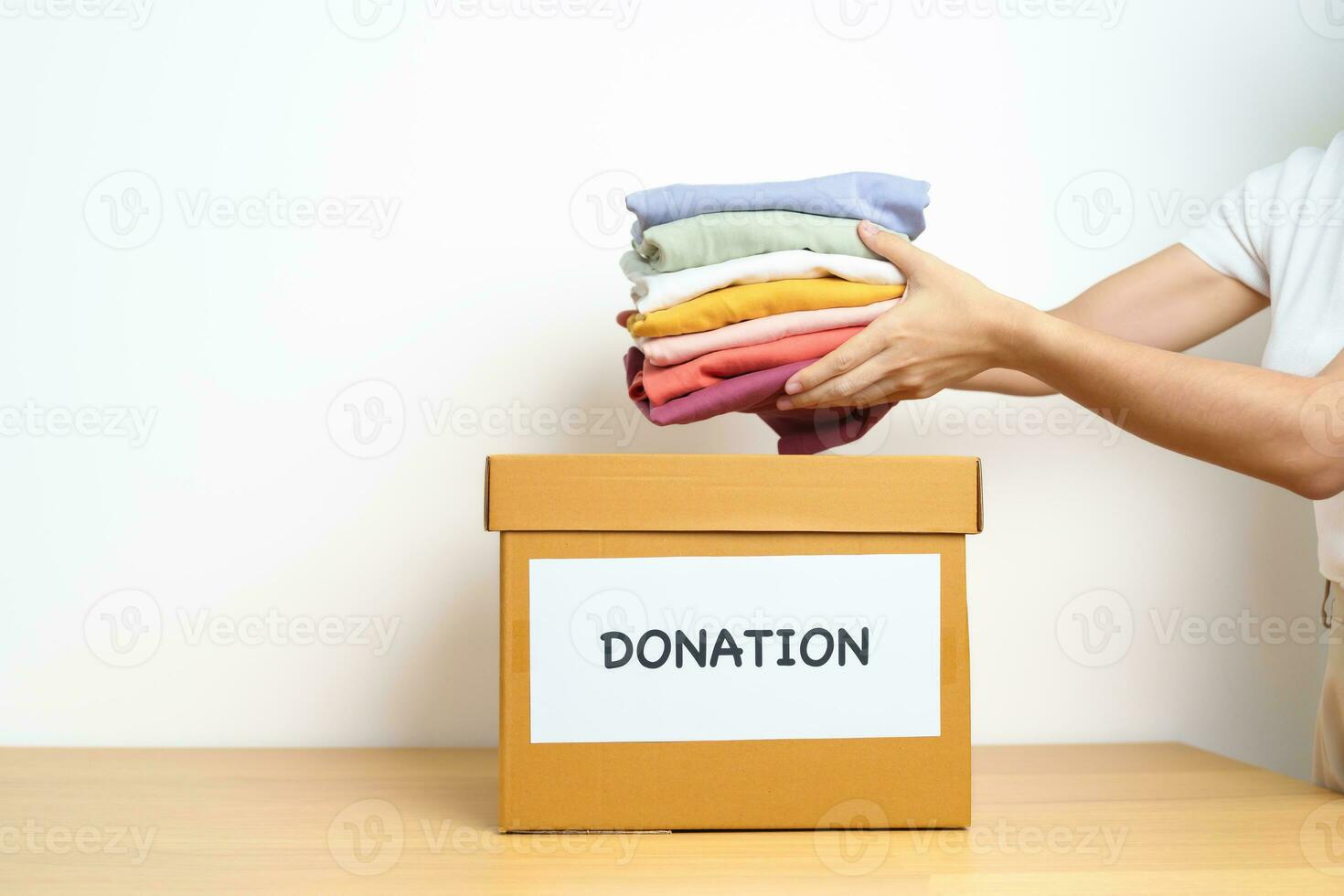 Donation, Charity, Volunteer, Giving and Delivery Concept. Hand holding Clothes into Donation box at home or office for support and help poor, refugee and homeless people. Copy space for text photo