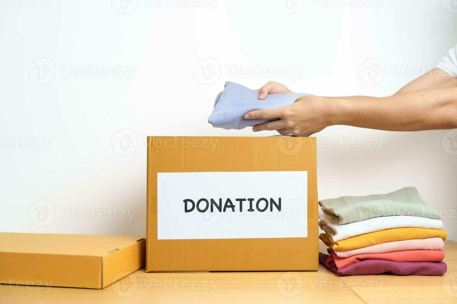 Donation, Charity, Volunteer, Giving and Delivery Concept. Hand holding Clothes into Donation box at home or office for support and help poor, refugee and homeless people. Copy space for text photo