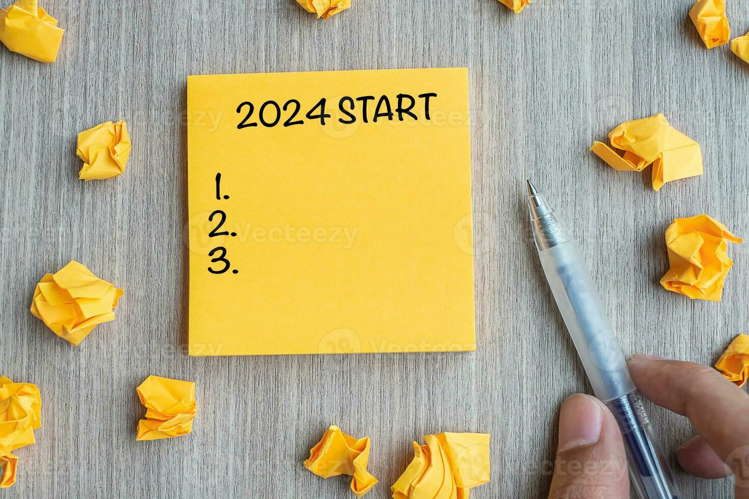 2024 Start word on yellow note with Businessman holding pen and crumbled paper on wooden table background. New Year, Resolutions, Strategy and Goal concept photo