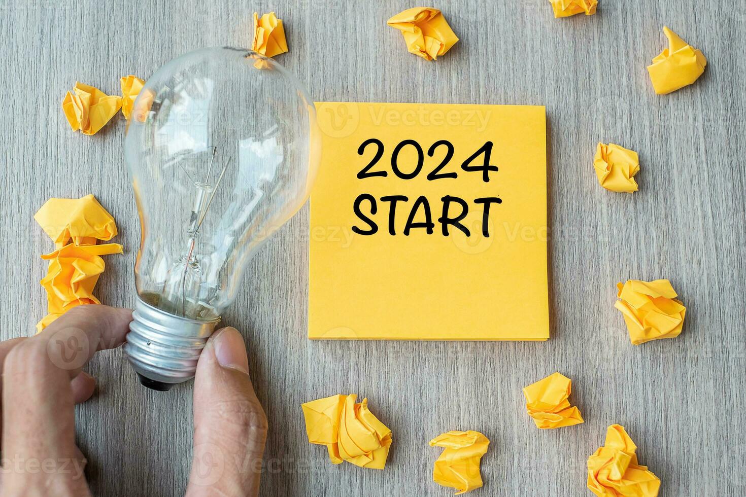 2024 Start words on yellow note and crumbled paper with Businessman holding lightbulb on wooden table background. New Year New Idea Creative, Innovation, Imagination, Resolution and Goal concept photo