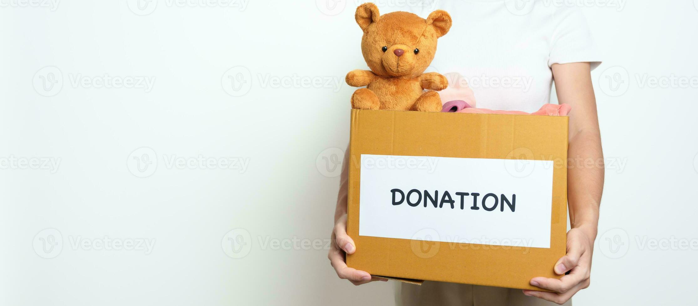 Kid Donation, Charity, Volunteer, Giving and Delivery Concept. Hand holding Bear doll and Clothes into Donation box at home for support and help poor, refugee and homeless people. Copy space for text photo