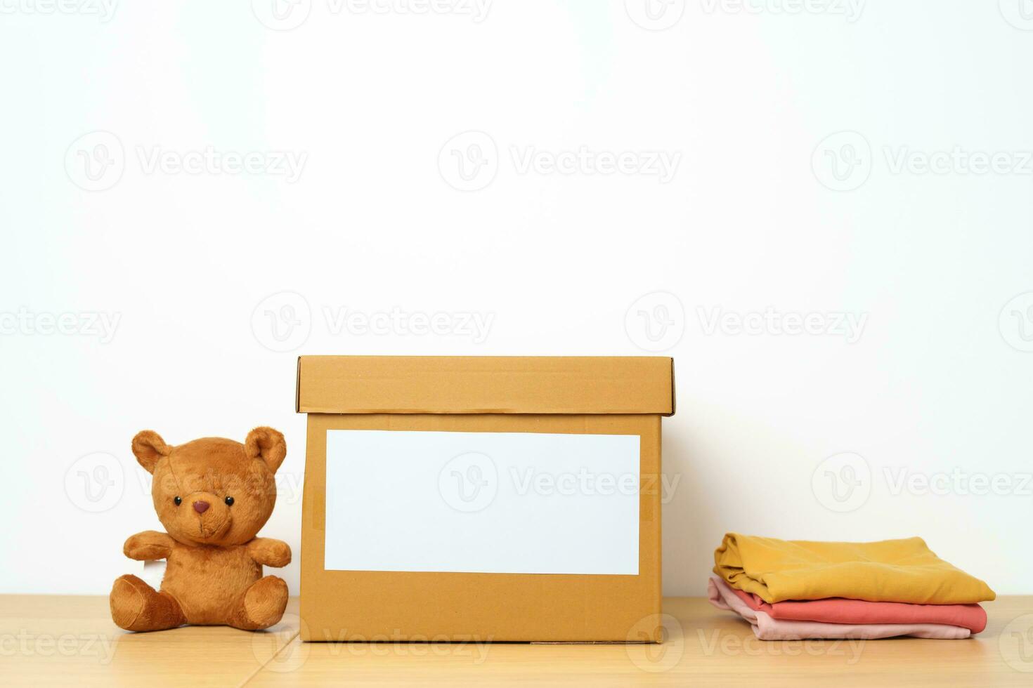 Kid Donation, Charity, Volunteer, Giving and Delivery Concept. Hand donate Bear doll and Clothes into cardboard box at home for support and help poor, refugee and homeless people. Copy space for text photo