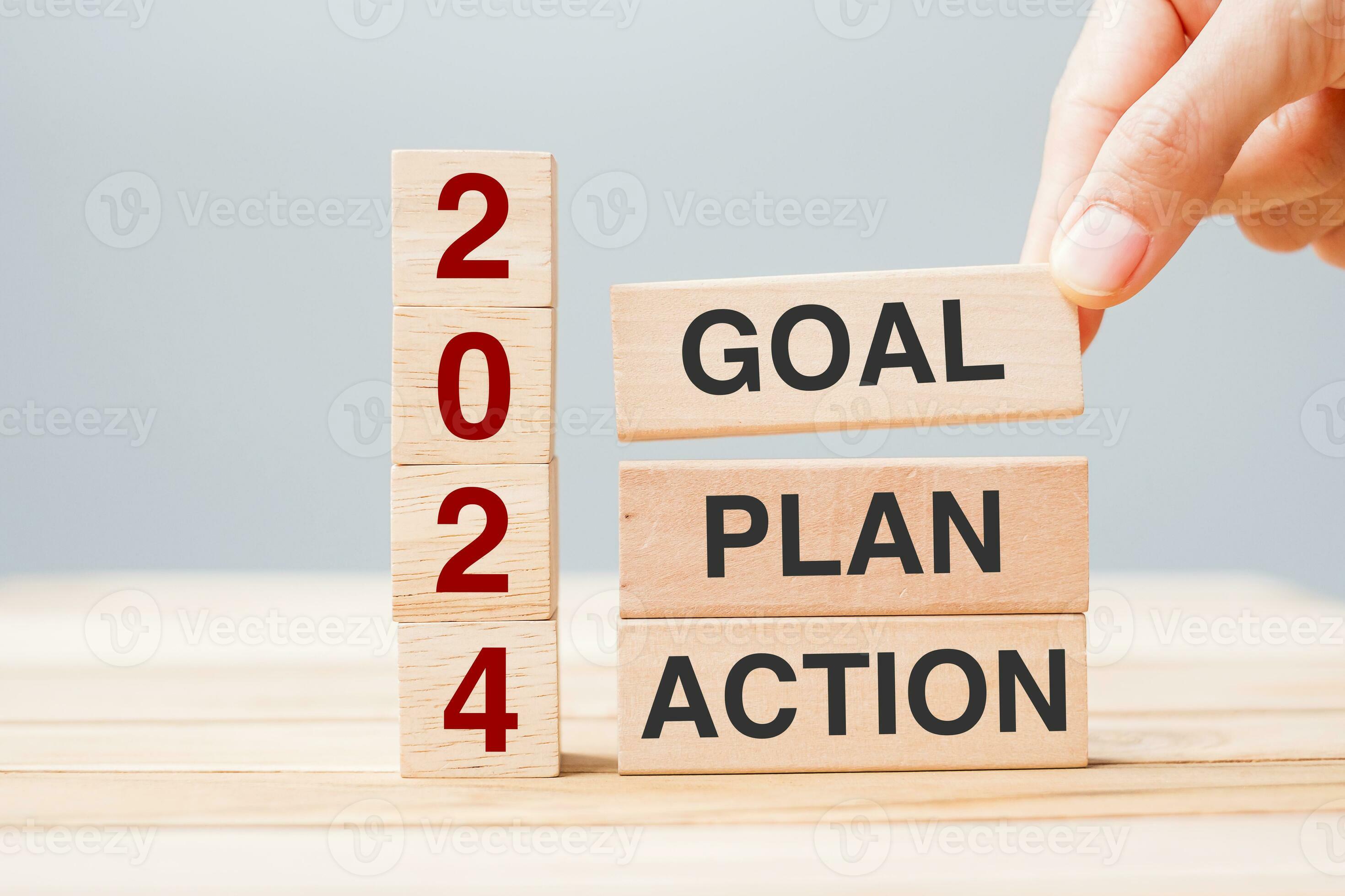 hand holding wooden block with text 2024 GOAL, PLAN and ACTION on table