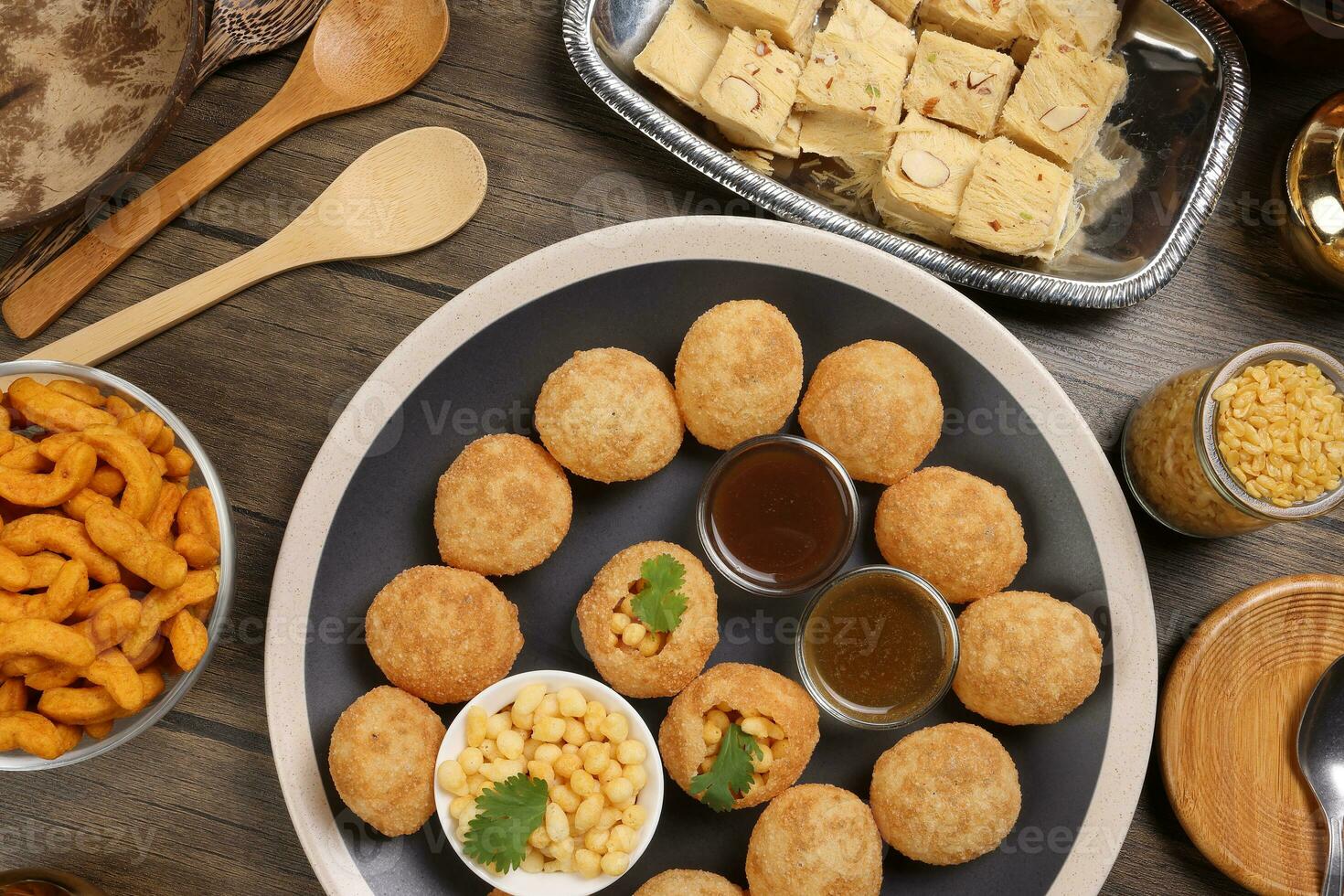 verity of indian bengali street food tea time snacks onion pakoda crunchy spicy lentils moong dal fry sweet shompapri chaat pani puri fuska on rustic retro table plate brass copper pots silver tray photo