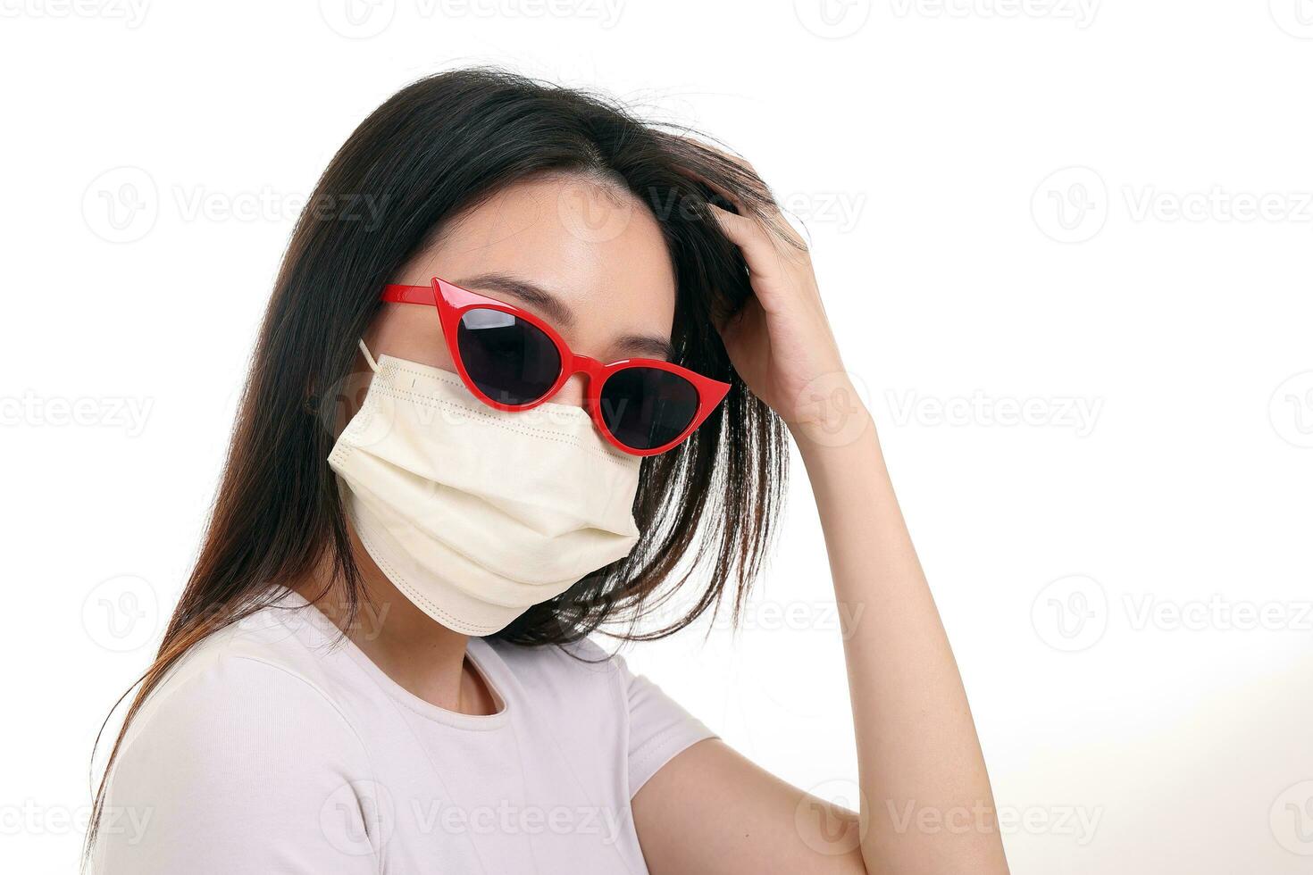 Beautiful young south east Asian woman wearing red frame dark sunglass three ply anti virus surgical face mask pose fashion style white background hand in hair photo