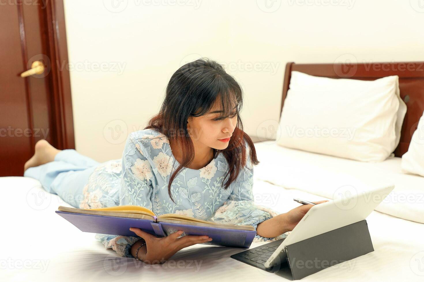 young Asian Malay Muslim woman wearing baju kurung dress at home on bed study work on computer tab book notebook pen read write photo