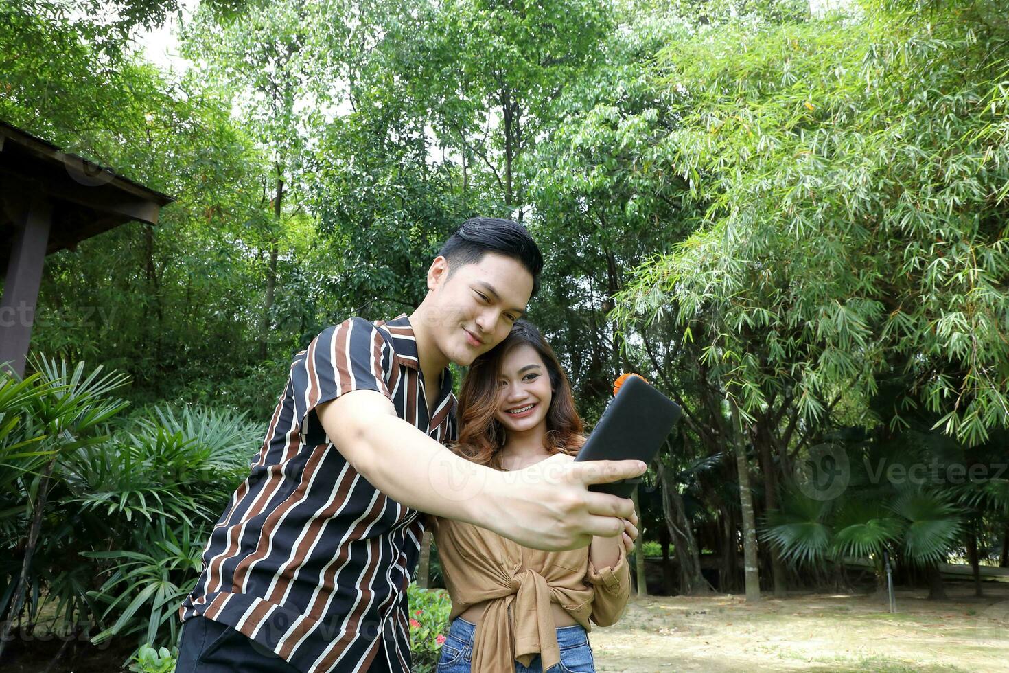 Young Asian Malay man woman outdoor green park walk talk discuss mingle under umbrella photo