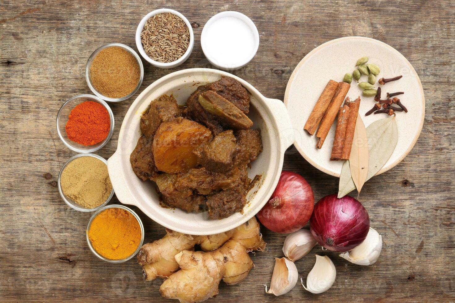 Beef bhuna dry curry with potato in ceramic bowl ingredients chilli cumin coriander turmeric powered salt onion garlic ginger bay leaf cinnamon cardamom clove over rustic wood background photo