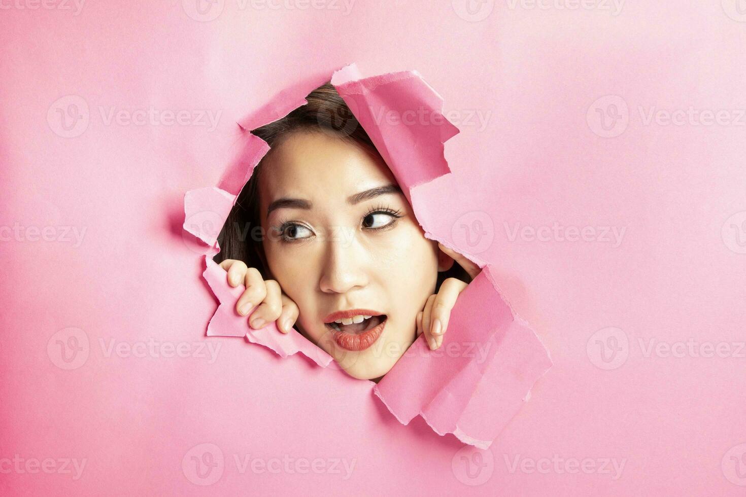 Young beautiful Asian woman expression through torn paper hole photo